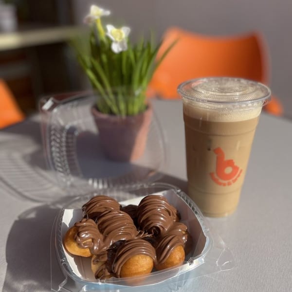 Ballers & Brew iced coffee and chocolate-drizzled donut holes on a table with a plant.