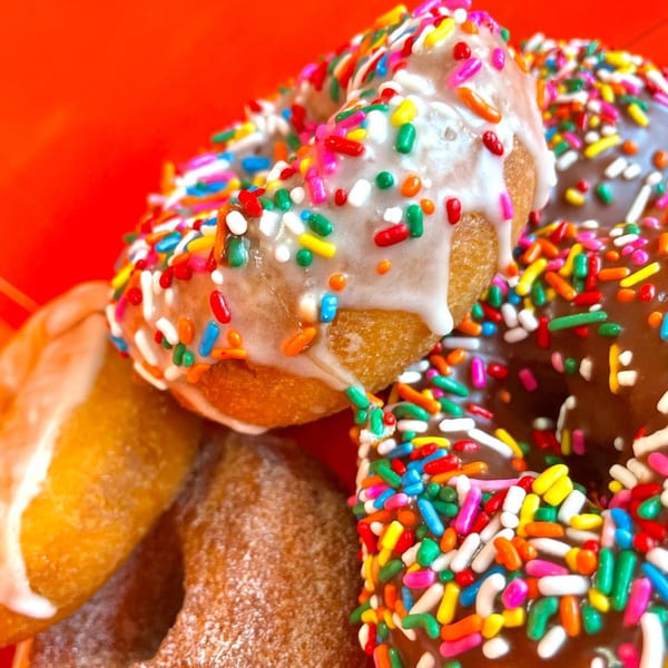 Close-up of assorted donuts with colorful sprinkles and white or chocolate icing, against a red background.